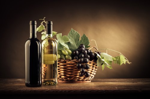 Ảnh chai rượu vang, trái nho và lá trong giỏ trên một chiếc bàn gỗ mộc mạc