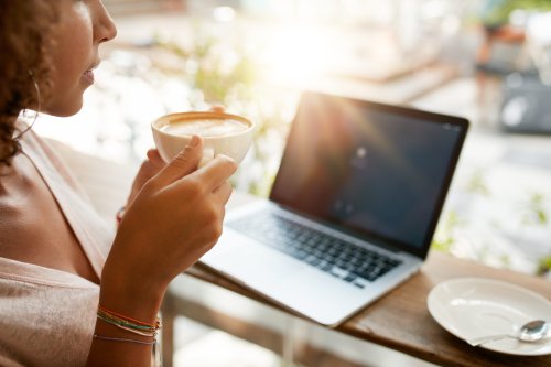 Hình ảnh người phụ nữ uống cà phê với một máy tính xách tay trên bàn tại nhà hàng.