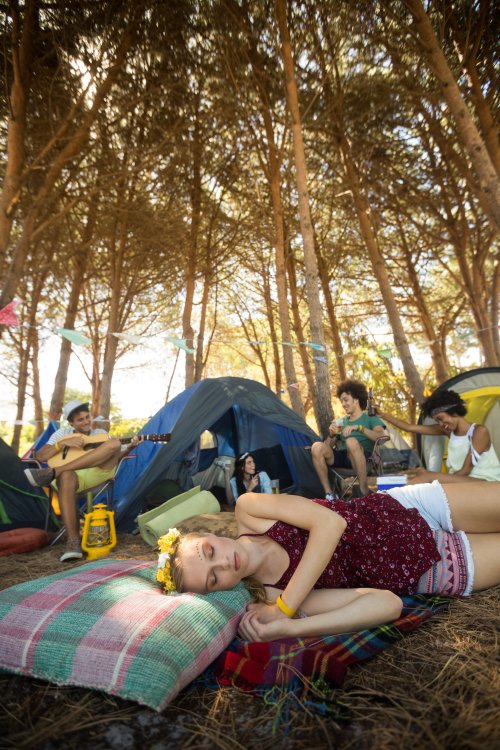 Ảnh chụp Người phụ nữ trẻ đang ngủ trong khi bạn bè vui vẻ tại khu cắm trại
