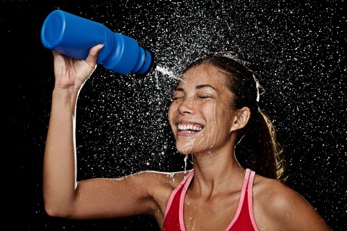 Hình ảnh Người phụ nữ tập thể dục uống nước và bắn tung tóe nước vào mặt cô. hình ảnh hài hước của mô hình thể dục thẩm mỹ nữ xinh đẹp trên nền đen.